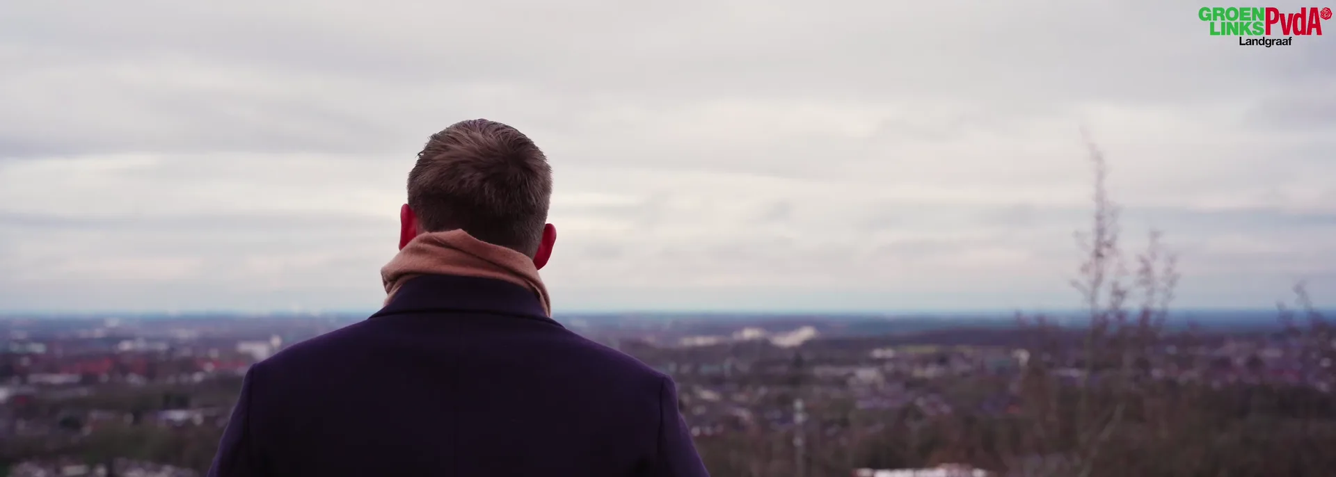 Een man van achteren op een heuvel, uitkijkend over Landgraaf.