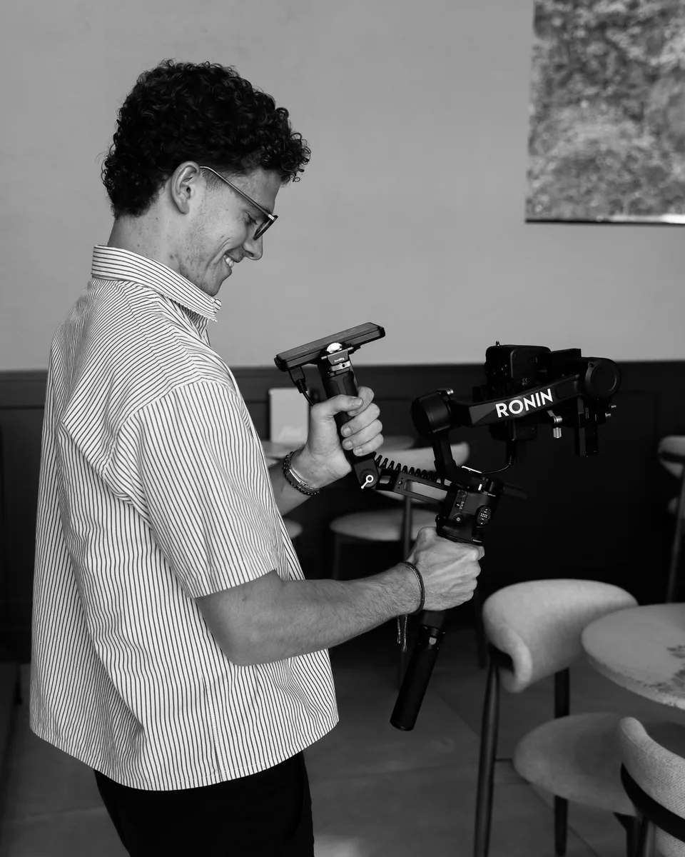 Maarten van Schijndel lacht terwijl hij zijn camera op een gimbal bedient. Zwart-wit.